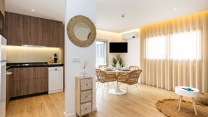 Una cocina moderna con armarios de madera, un comedor con una mesa redonda y sillas de mimbre, y una sala de estar con televisor y cortinas.