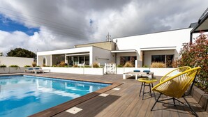 Un espace piscine extérieur moderne, doté d’une terrasse en bois, d’un bâtiment blanc et de chaises jaunes.