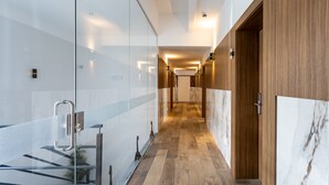 Un couloir moderne avec des murs en verre, un plancher en bois et un mur d’accent en marbre.
