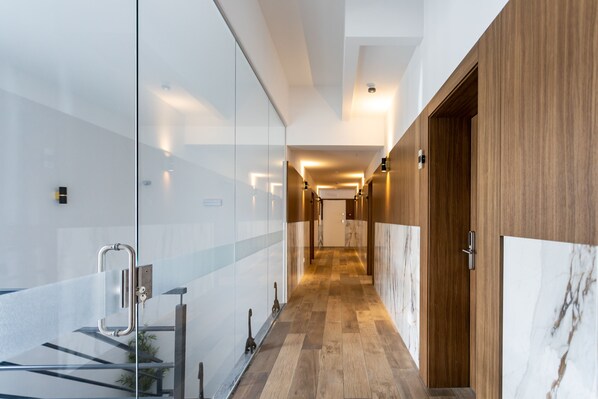 A modern hallway with glass walls, wooden flooring, and a marble accent wall. - Marinha Grande apartamentos N°5 ICE (Marinha Grande)