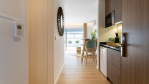 A modern kitchen with wooden cabinets, a built-in microwave, and a dining area with a chair and table. - Marinha Grande apartamentos  N°5 ICE (Marinha Grande)