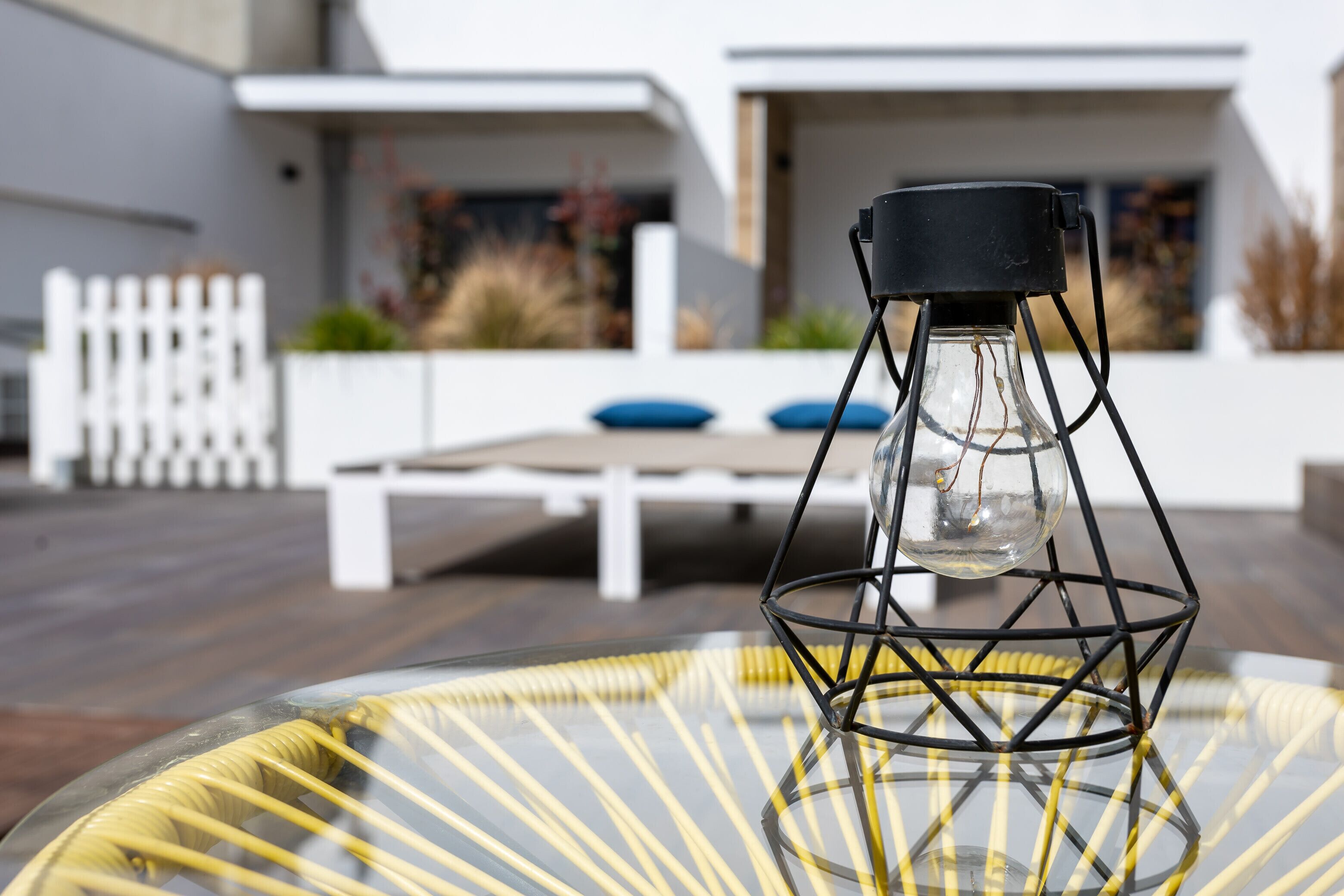 A modern outdoor seating area with a glass table and a unique black metal lamp.