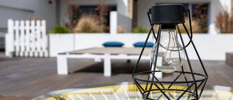 A modern outdoor seating area with a glass table and a unique black metal lamp.