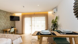 A hotel room with a bed, a desk, a dining table set with plates and glasses, and a TV mounted on the wall. - Marinha Grande apartamentos  N°5 ICE (Marinha Grande)