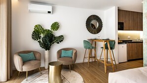 A modern living room with a sofa, chairs, a coffee table, a large plant, and a kitchen area with wooden cabinets and a refrigerator. - Marinha Grande apartamentos  N°5 ICE (Marinha Grande)