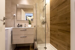A modern bathroom with a wooden wall, a glass shower enclosure, and a vanity with drawers. - Marinha Grande apartamentos  N°5 ICE (Marinha Grande)