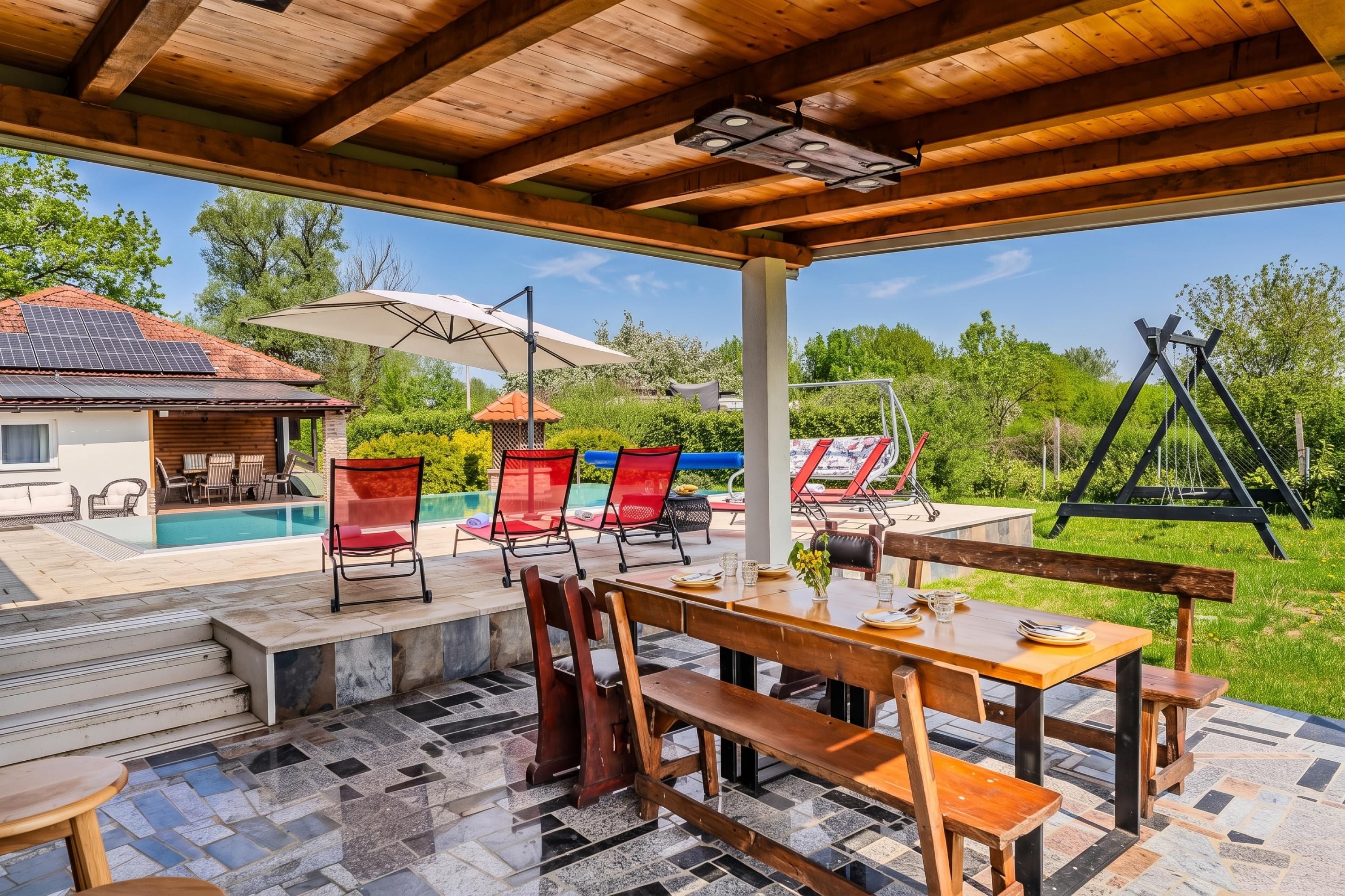 Katettu ulkoalue, jossa on uima-allas, puiset huonekalut ja näkymä ympäröivään vihreään maisemaan.