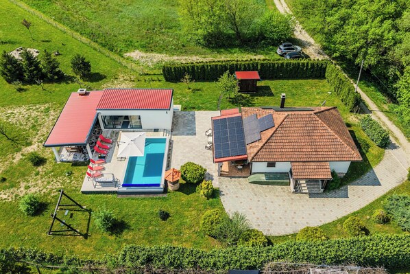 Vue aérienne d’une propriété dotée d’une piscine, d’un bâtiment au toit rouge et de panneaux solaires.