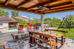 Un espace extérieur abrité, doté d’une piscine, de mobilier en bois et offrant une vue sur la verdure environnante.