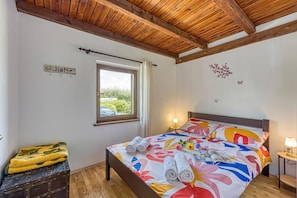 A bedroom with a bed, a window, a wooden ceiling, a small table with a lamp, and a decorative wall piece. - Wellness House On The River Kupa (Karlovac)