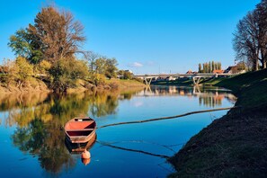 Een rustige rivier met een klein bootje aan de linkerkant, een brug op de achtergrond en bomen langs de oever.