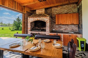 Un espace repas doté d’un four en briques, de meubles en bois et offrant une vue sur l’extérieur.