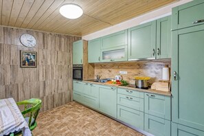 Una cocina con paredes de madera, armarios verdes, un reloj y una mesa con una silla.