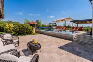 Un espace aménagé au bord de la piscine, avec des chaises longues, une petite table décorée de fleurs et une pergola ombragée par des parasols.