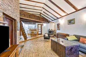 A spacious living area with a wooden floor, a sofa, a coffee table, a fireplace, and a staircase leading to an upper level.