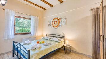 A bedroom with a bed, a window with curtains, a bedside lamp, and a wall art piece.