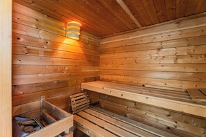 Un sauna en bois, doté de bancs et d’un luminaire fixé au mur.