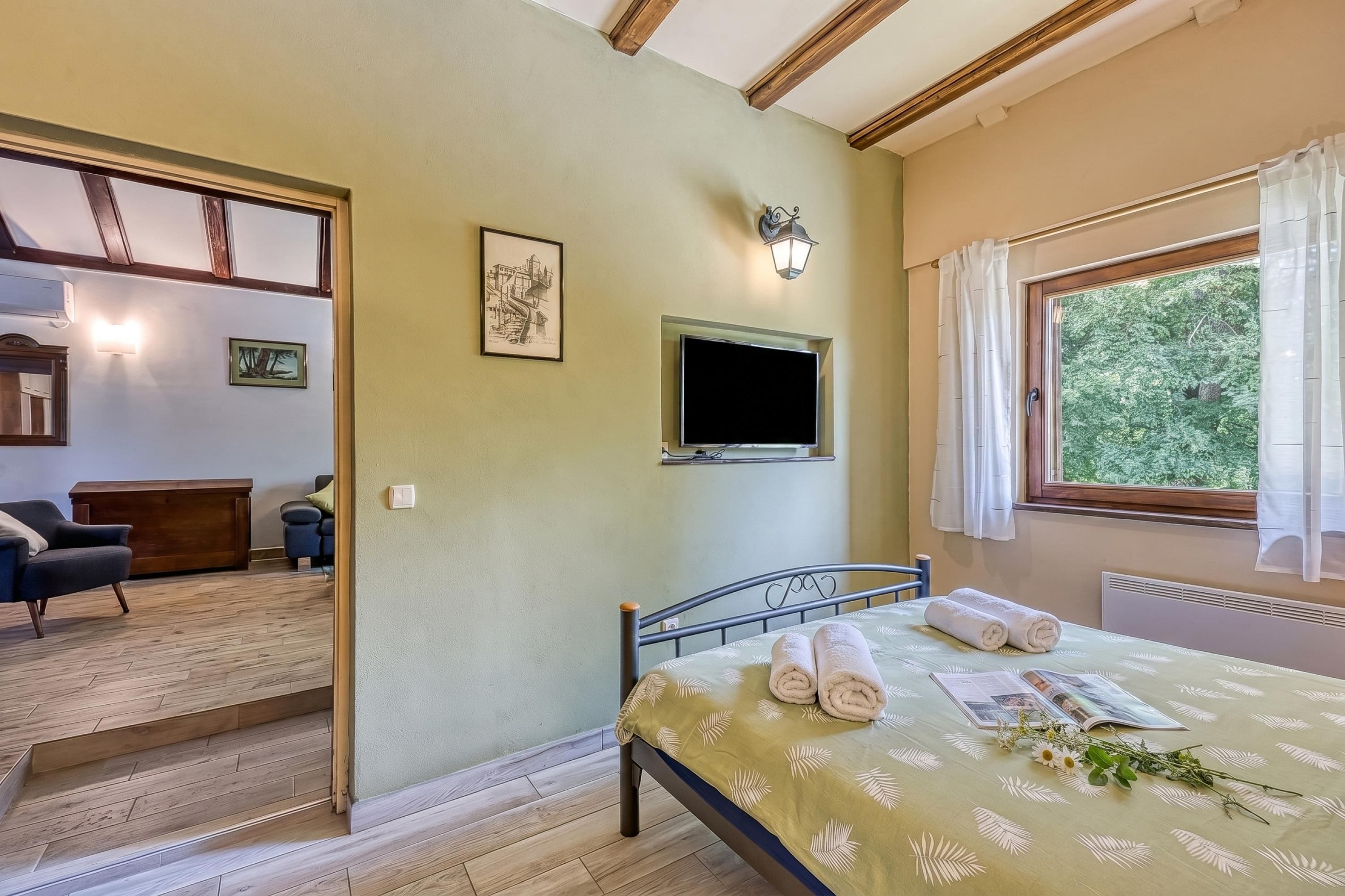 A bedroom with a bed, a TV, a window, and a staircase leading to another room.