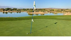 A golf course with a flagstick, water body, and distant mountains. - La Estrella 10, Desert Springs Golf Resort (Cuevas del Almanzora, Almería)