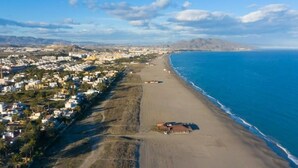 An aerial view of a coastal area with a beach, residential buildings, and a clear sky. - La Estrella 10, Desert Springs Golf Resort (Cuevas del Almanzora, Almería)