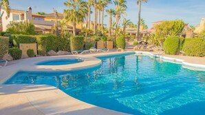 A swimming pool with a curved edge, surrounded by palm trees and a building in the background. - La Estrella 10, Desert Springs Golf Resort (Cuevas del Almanzora, Almería)