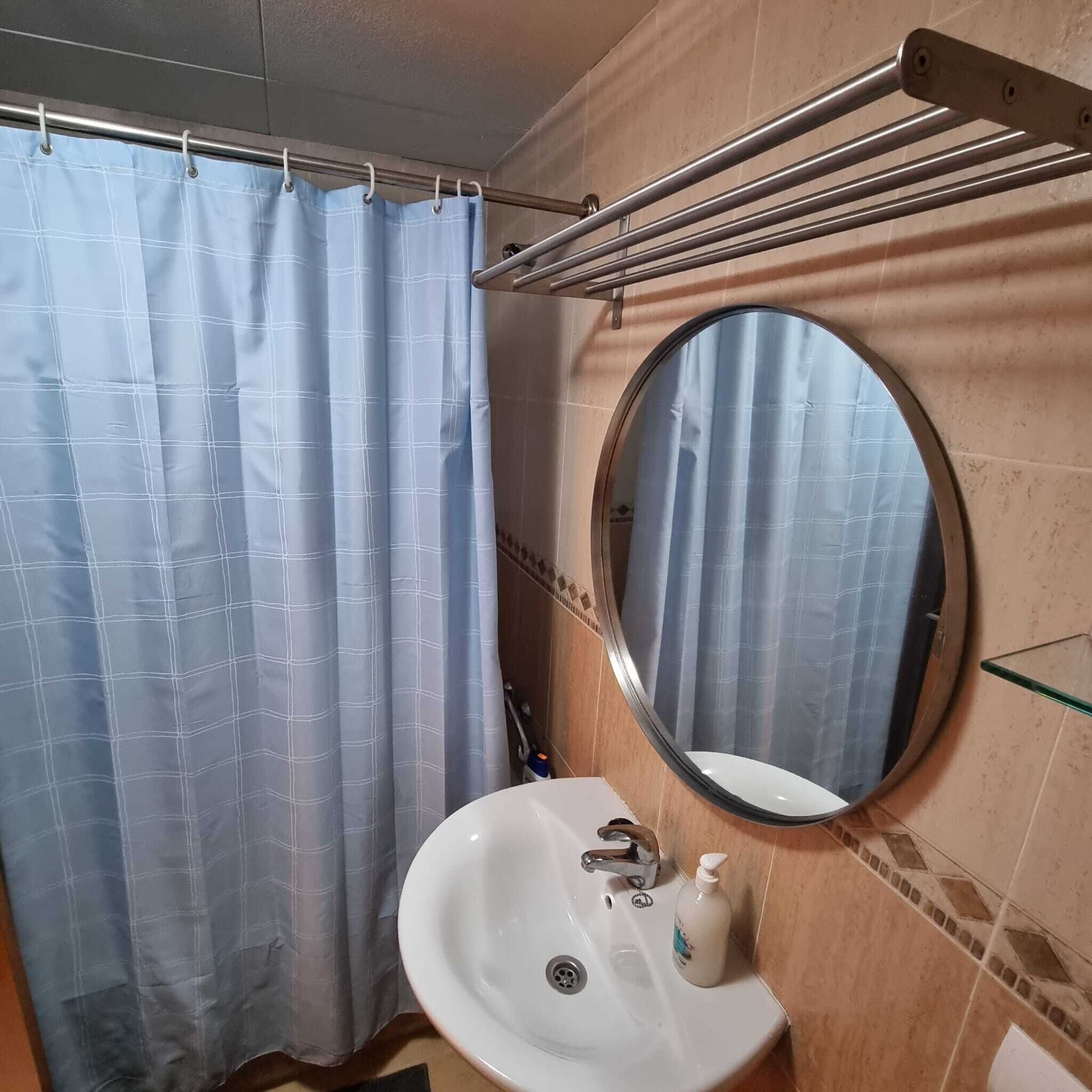 A bathroom with a shower curtain, a round mirror, a sink, and a towel rack.