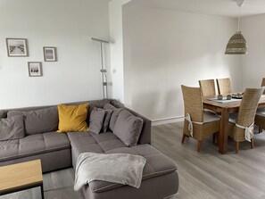 A modern living room with a grey sectional sofa, a dining table with wicker chairs, and a hanging light fixture.