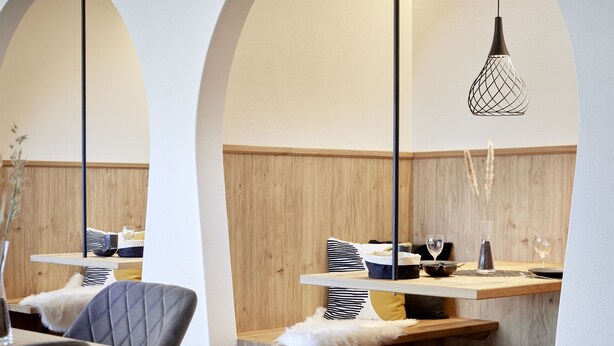 A modern interior with wooden panel walls, a central dining table, and a hanging light fixture. - Maximilian Appartements (Schwangau)