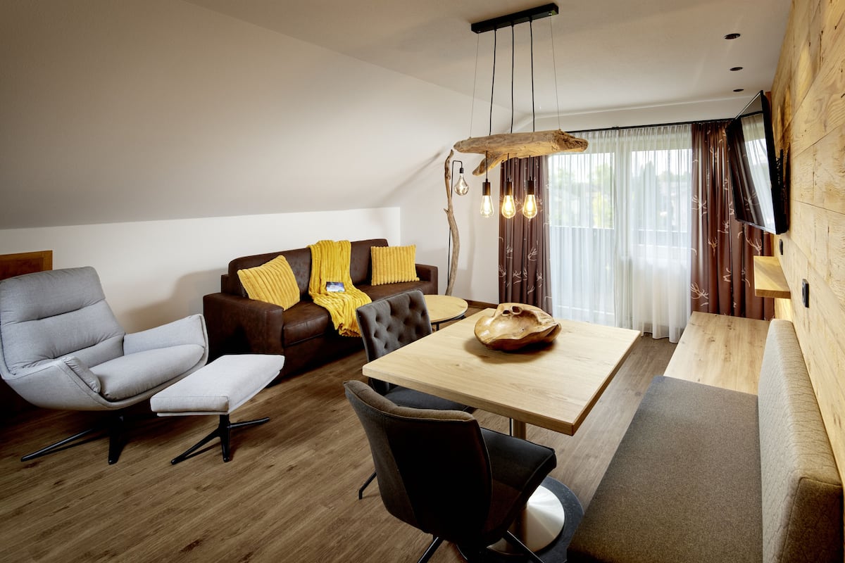 A modern living room with a grey armchair, a brown sofa with yellow cushions, a wooden dining table, and a black chair.