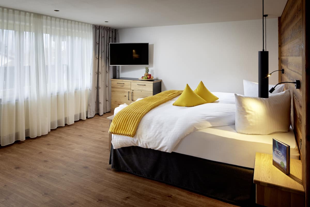 A modern hotel room with a large bed, wooden floor, a flat-screen TV, and a wooden nightstand.