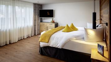 Ein modernes Hotelzimmer mit einem großen Bett, Holzboden, einem Flachbildfernseher und einem Nachttisch aus Holz.