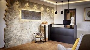 A reception area with a stone wall, a wooden reception desk, a laptop, and a decorative sculpture. - Maximilian Appartements (Schwangau)