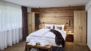A modern hotel room with a wooden wall panel, a large bed with white linens, a wooden nightstand, and a wooden wardrobe. - Maximilian Appartements (Schwangau)