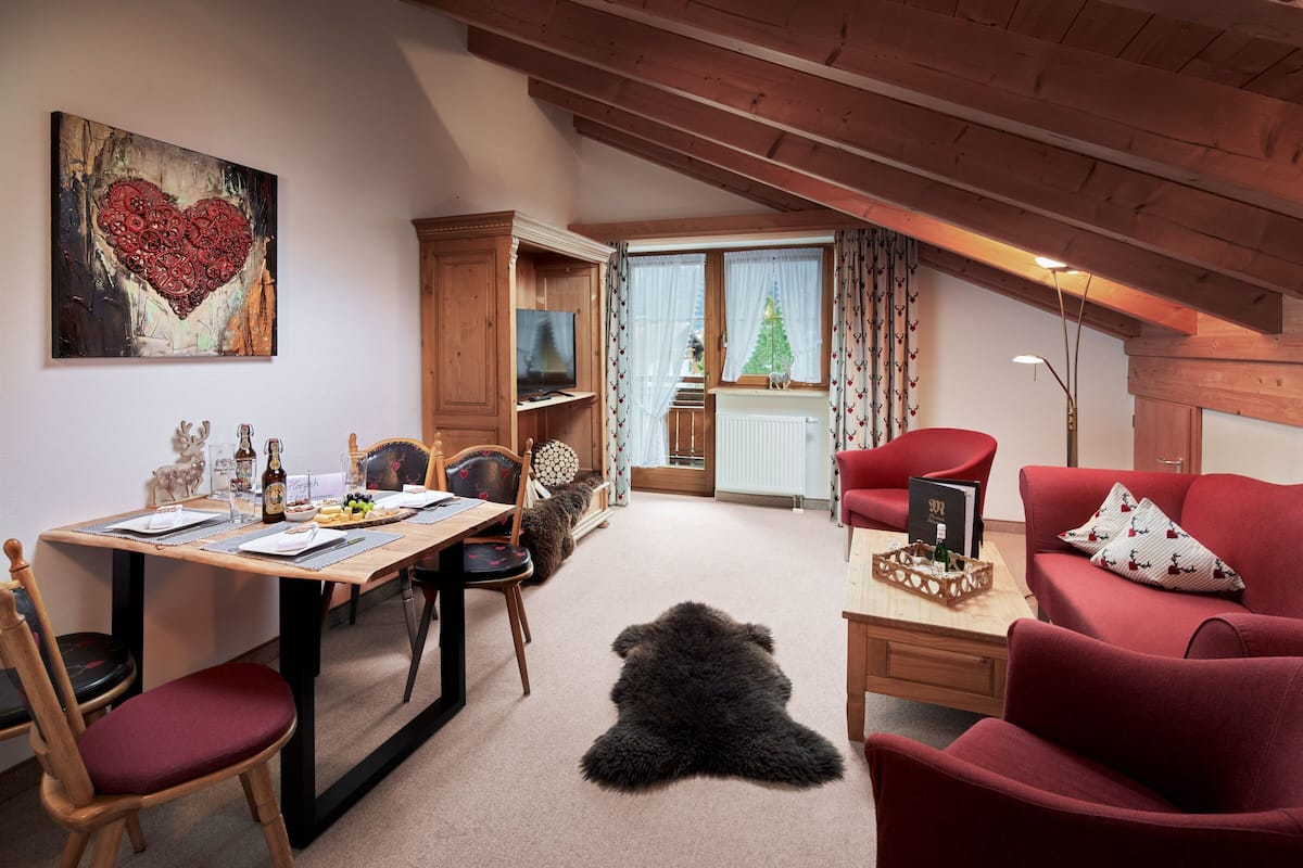 A cozy room with a dining table, chairs, a red sofa, a fur rug, a television, and a heart-themed artwork on the wall.
