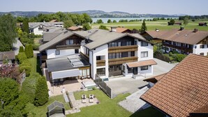 A modern residential building with a spacious patio, a swimming pool, and a view of a lake and mountains. - Maximilian Appartements (Schwangau)