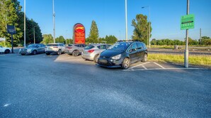 Un estacionamiento con coches, un cartel rojo con un logotipo amarillo y un cartel informativo verde.