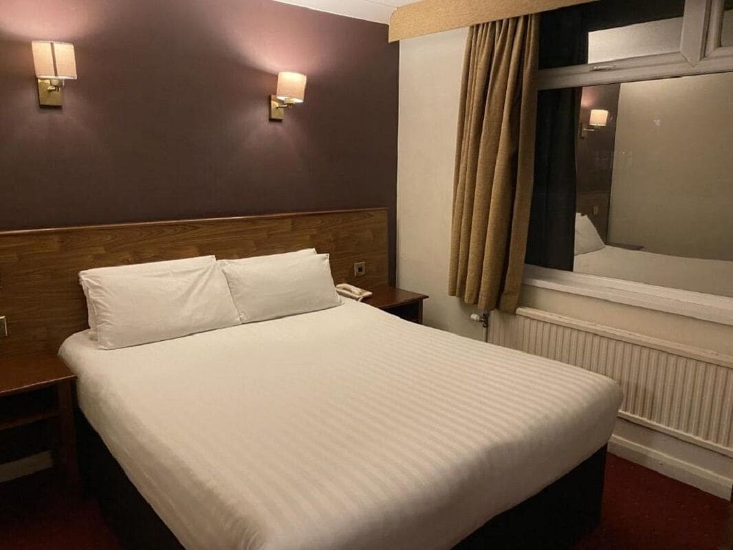 Habitación de hotel con una cama grande, dos mesitas de noche, un cabecero de madera y dos lámparas fijadas a la pared.