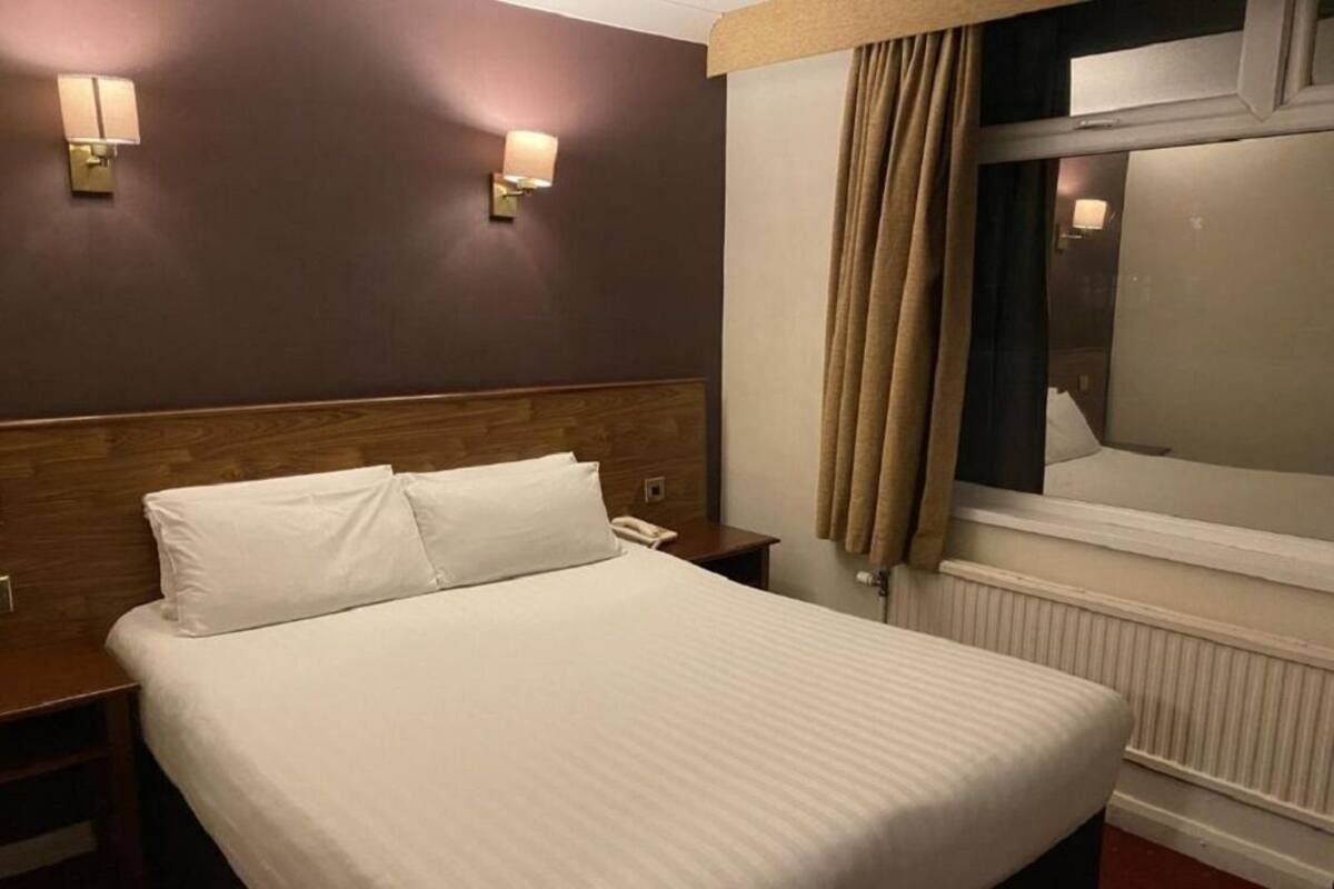A hotel room with a large bed, two bedside tables, a wooden headboard, and two wall-mounted lamps.