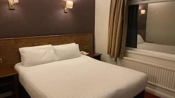 A hotel room with a large bed, two bedside tables, a nightstand, a window with curtains, and wall-mounted lamps.