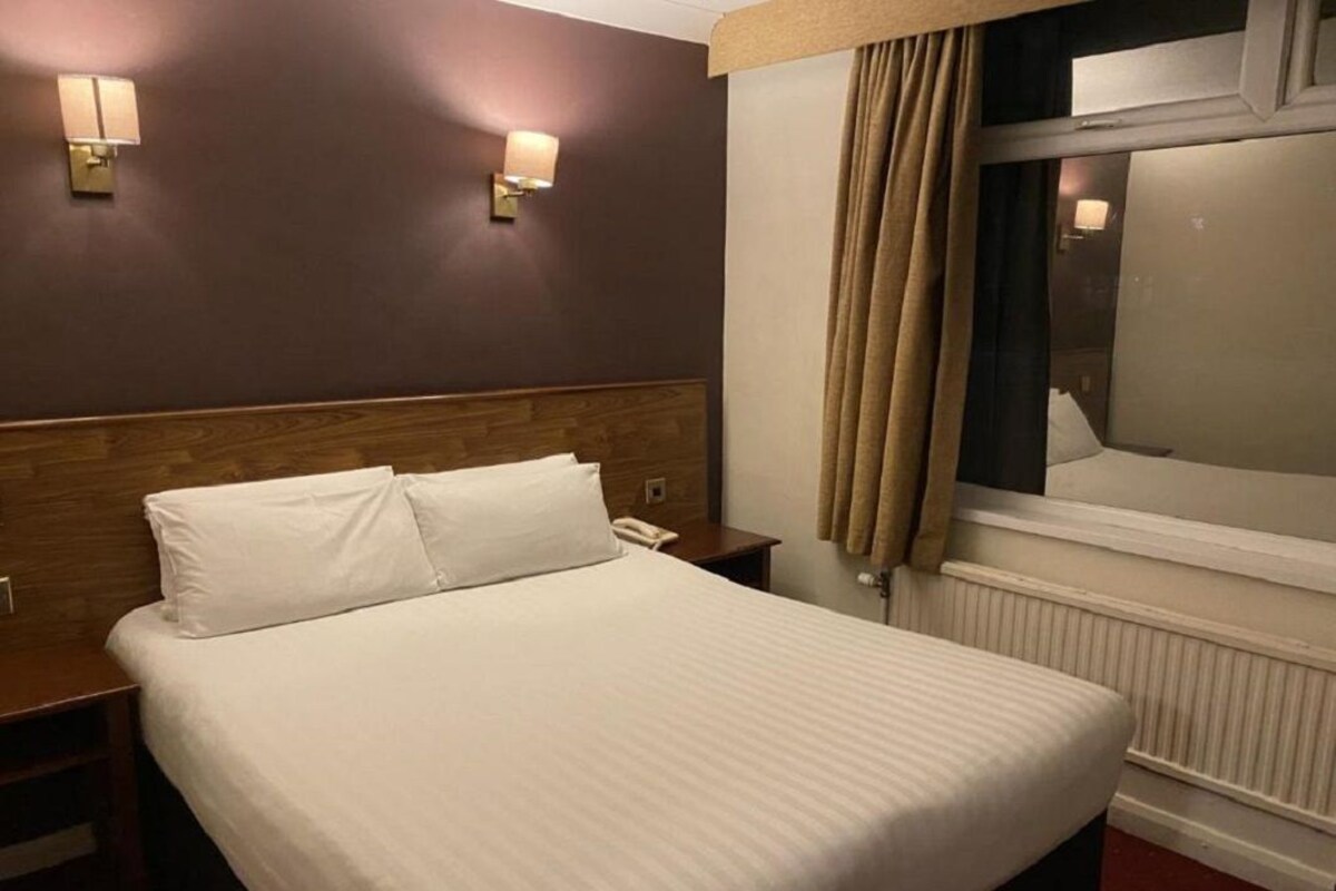 A hotel room with a large bed, two bedside tables, a wooden headboard, and two wall-mounted lamps.