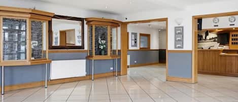 A hotel lobby with a reception desk, a waiting area with a bench, and a tiled floor.