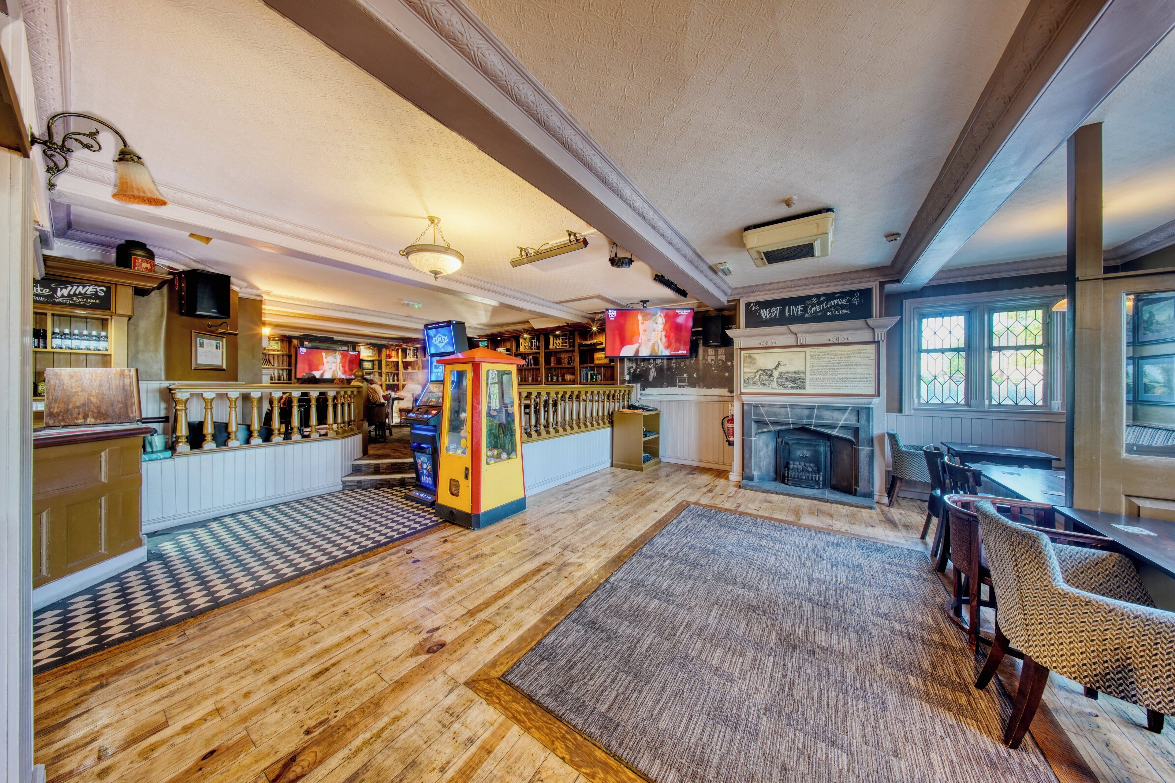 A bar area with a fireplace, wooden flooring, and a seating area with tables and chairs.