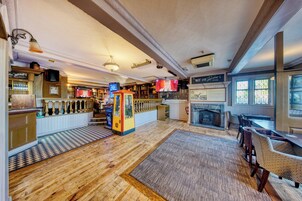 A bar area with a fireplace, wooden flooring, and a seating area with tables and chairs.
