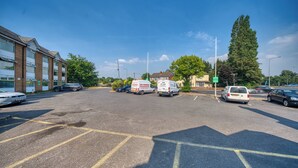 Um estacionamento com vários carros e um edifício com grandes janelas à esquerda.