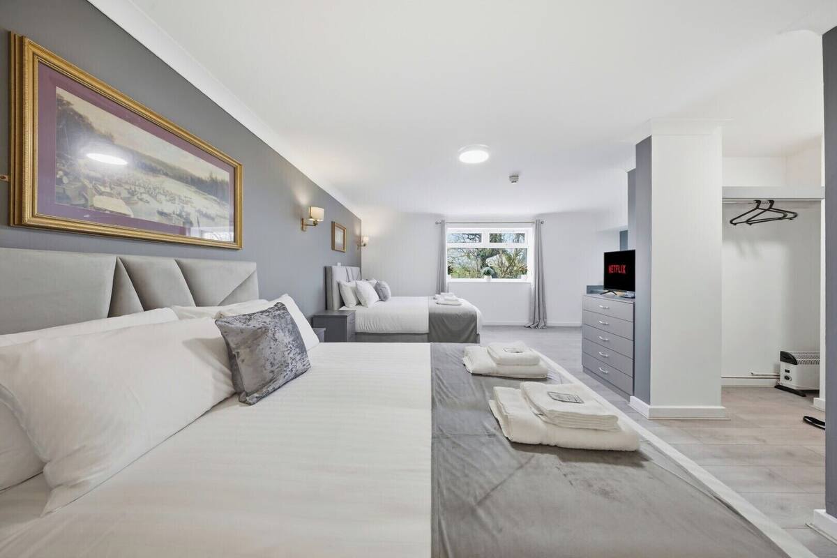 A modern hotel room with a large bed, a smaller bed, a desk, a television, and a window with a view of greenery.