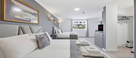 A modern hotel room with a large bed, a smaller bed, a desk, a television, and a window with a view of greenery.