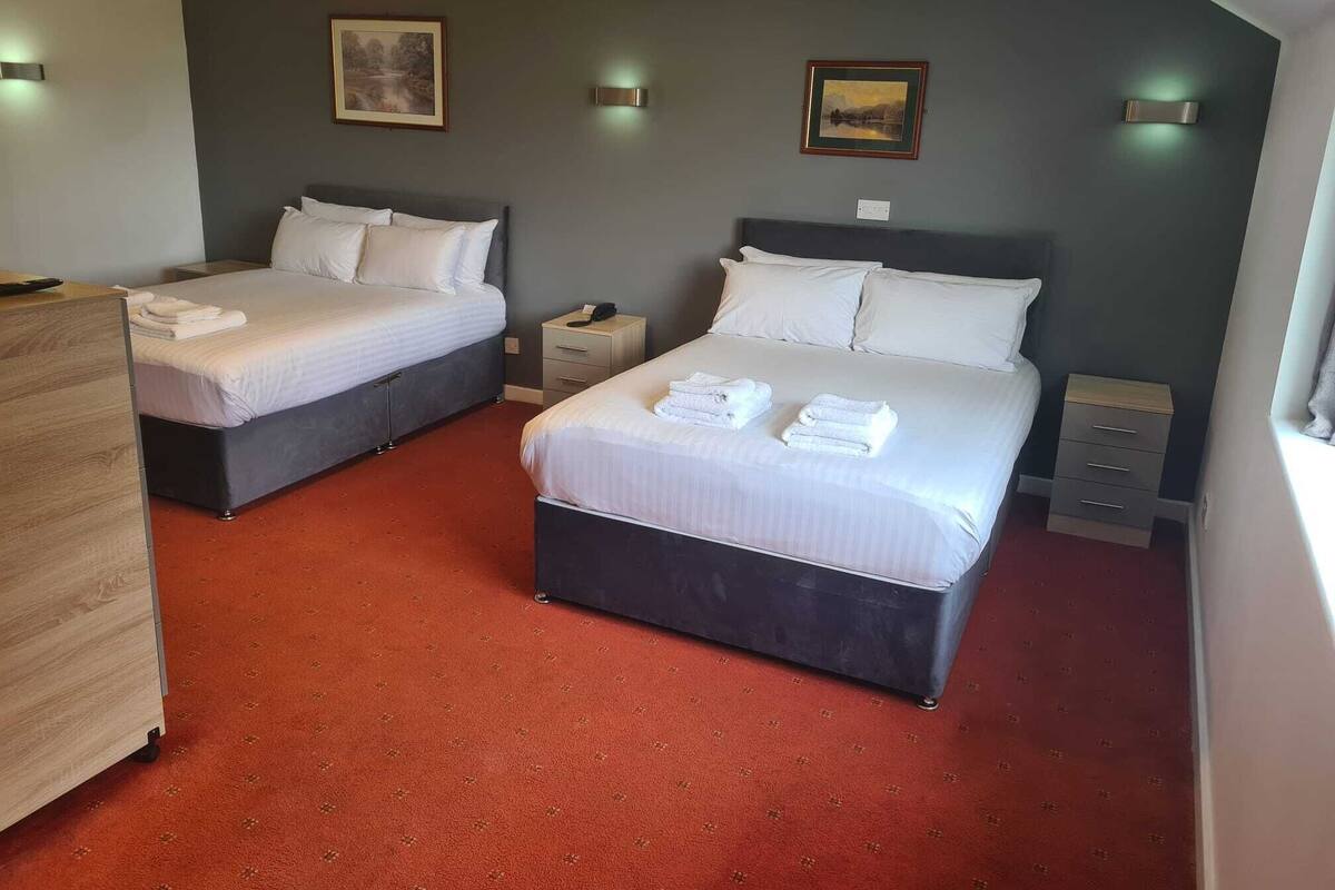 A hotel room with two beds, a desk, a chair, and a window.