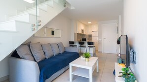 Un salon moderne avec un canapé, une table basse et un téléviseur. Un escalier mène à l’étage supérieur.