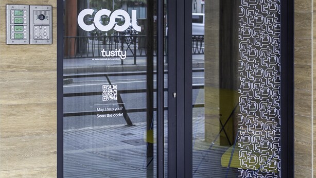 L’entrée d’un hôtel, avec une porte en verre, un code QR et un panneau indiquant le numéro de chambre 334.