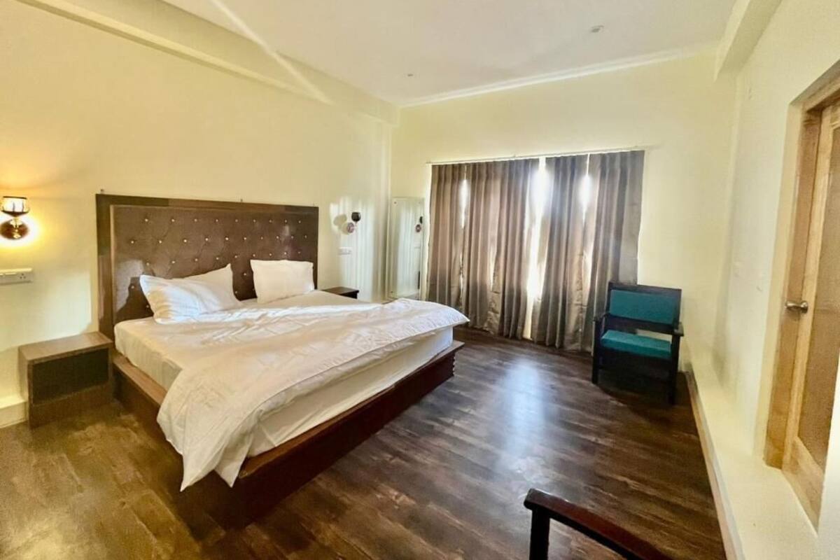 A bedroom with a large bed, a bedside table, a chair, a window with curtains, and a door.